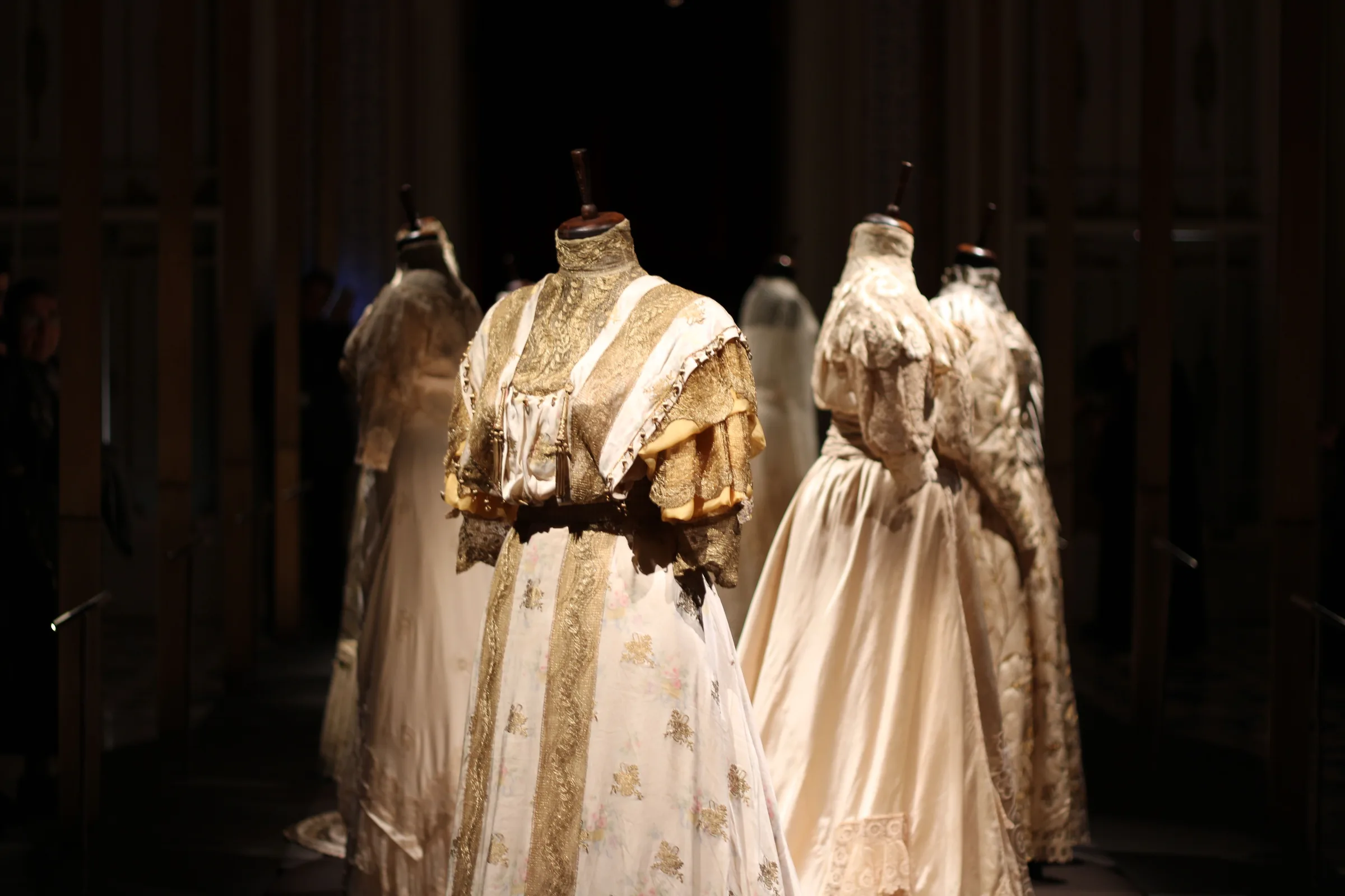 Couture garments displayed on dress forms in a dark exhibition setting.
